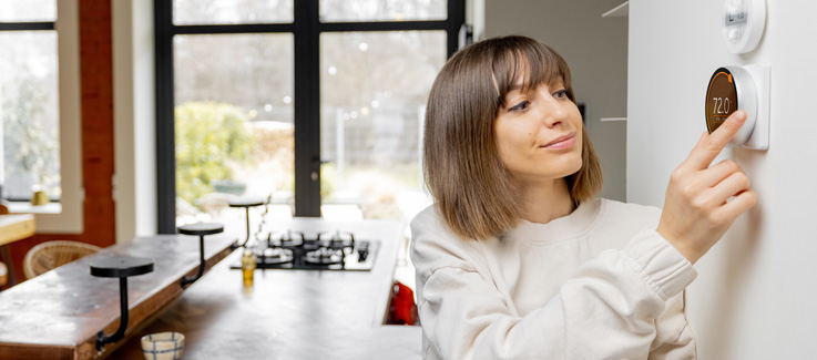 A woman adjusting her thermostat.