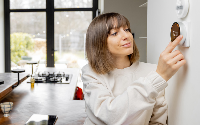 A woman adjusting her thermostat.