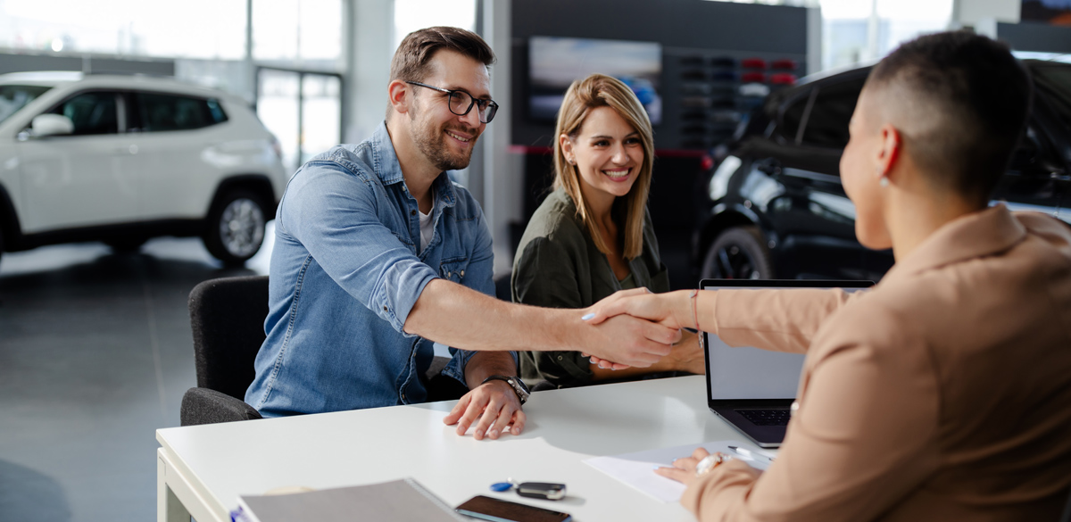 Couple shaking hands with lender at car dealership