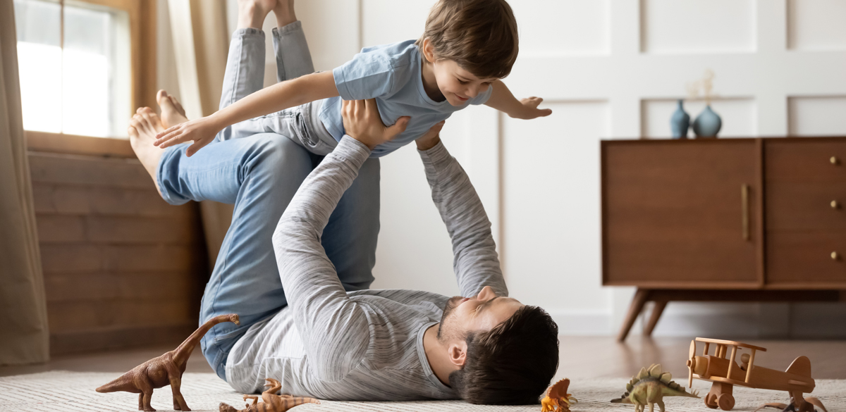 Boy playing airplane with his father on the floor