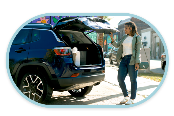 A woman smiling while looking at shopping bags in open hatchback of her blue SUV.